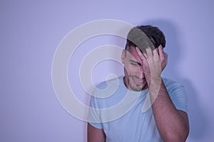 Young Hispanic male with hand on head and wincing in pain on white background