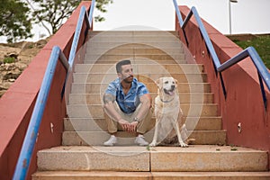 Young Hispanic male, sitting on stairs next to his dog as they both look in the same direction. Concept, dogs, pets, animals,