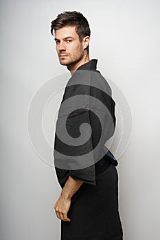 Young Hispanic male wearing a black kimano standing against a white wall