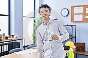 Young hispanic man architect smiling confident holding glasses at office