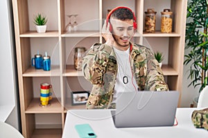 Young hispanic man army soldier using laptop and headphones at home