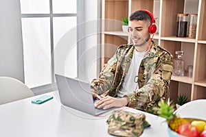 Young hispanic man army soldier using laptop and headphones at home