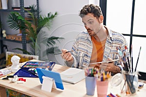 Young hispanic man artist having video call drawing at art studio photo