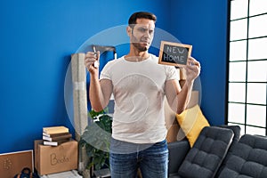 Young hispanic man with beard holding keys of new home clueless and confused expression