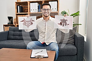 Young hispanic man with beard holding rorschach test smiling with a happy and cool smile on face