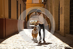 Young Hispanic man with beard and sunglasses with his dog holding on to the leash walking along a sunny street at sunset. Concept