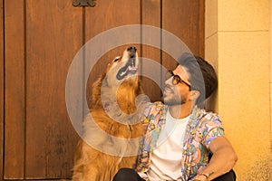 Young Hispanic man with beard and sunglasses sitting next to his dog on the front step of a house, very happy. Concept animals,