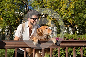 Young Hispanic man with beard, sunglasses and white shirt, leaning out with his dog leaning on a railing in funny attitude.