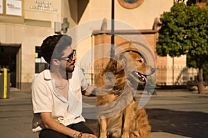 Young Hispanic man with beard, sunglasses and white shirt, sitting on a bench hugging and petting his dog. Concept animals, dogs,