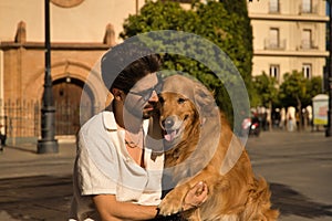 Young Hispanic man with beard, sunglasses and white shirt, sitting on a bench hugging and petting his dog. Concept animals, dogs,