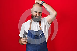 Young hispanic man with beard and tattoos wearing barber apron holding razor confuse and wondering about question