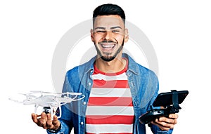 Young hispanic man with beard using drone with remote control smiling and laughing hard out loud because funny crazy joke