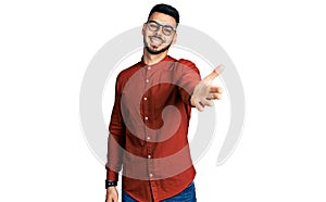 Young hispanic man with beard wearing business shirt and glasses smiling friendly offering handshake as greeting and welcoming