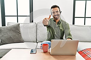 Young hispanic man with beard wearing call center agent headset working from home approving doing positive gesture with hand,