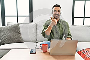 Young hispanic man with beard wearing call center agent headset working from home doing happy thumbs up gesture with hand