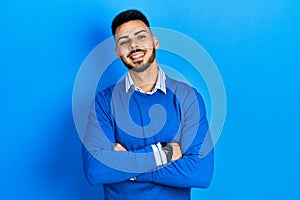 Young hispanic man with beard wearing casual blue sweater happy face smiling with crossed arms looking at the camera