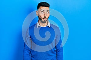 Young hispanic man with beard wearing casual blue sweater making fish face with lips, crazy and comical gesture