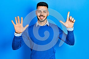 Young hispanic man with beard wearing casual blue sweater showing and pointing up with fingers number seven while smiling