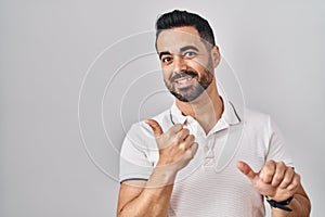 Young hispanic man with beard wearing casual clothes over white background pointing to the back behind with hand and thumbs up,