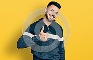 Young hispanic man with beard wearing casual winter sweater doing happy thumbs up gesture with hand