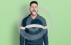 Young hispanic man with beard wearing casual winter sweater sticking tongue out happy with funny expression