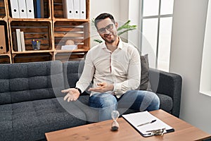 Young hispanic man with beard working at consultation office inviting to enter smiling natural with open hand