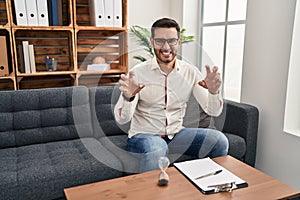 Young hispanic man with beard working at consultation office smiling funny doing claw gesture as cat, aggressive and sexy