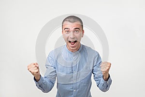 Young hispanic man in blue shirt celebrating victory of his team over gray background