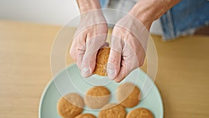 Young hispanic man breaking cookie with hands at dinning room