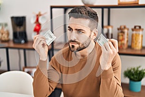Young hispanic man breaking dollar sitting on table at home