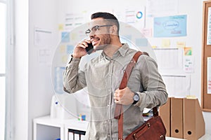 Young hispanic man business worker talking on smartphone holding briefcase at office