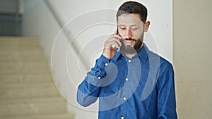 Young hispanic man business worker talking on smartphone smiling at the office