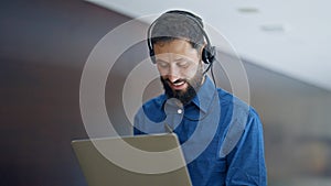 Young hispanic man business worker using laptop and headphones smiling at the office