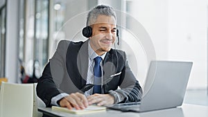 Young hispanic man business worker using laptop and headphones smiling at office
