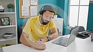 Young hispanic man business worker using laptop and headphones taking notes at the office