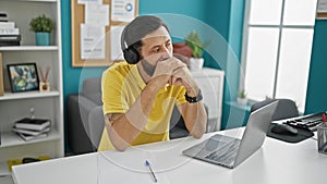 Young hispanic man business worker using laptop and headphones thinking at the office