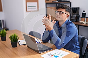 Young hispanic man business worker using laptop with serious expression at office