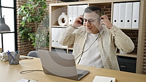 Young hispanic man business worker using laptop wearing headphones at office