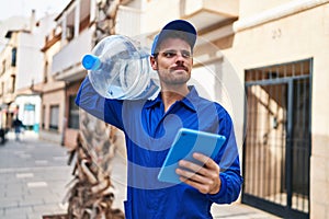 Young hispanic man courier holding water bottle using touchpad at street
