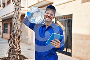 Young hispanic man courier holding water bottle using touchpad at street