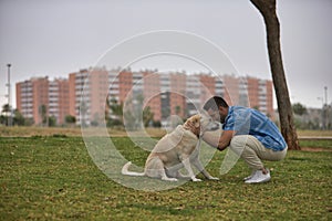 Young Hispanic man, crouching on the grass joining his forehead with his dog's forehead in loving and tender attitude.