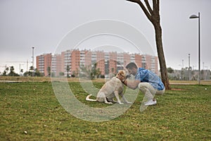 Young Hispanic man, crouching on the grass joining his forehead with his dog's forehead in loving and tender attitude.