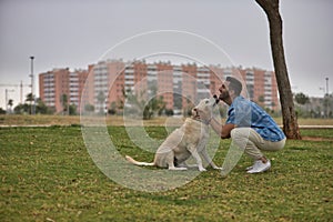 Young Hispanic man, crouching on the grass next to his dog while licking his face in a loving and tender attitude. Concept, dogs,