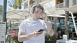 Young hispanic man dancing listening to music on smartphone at coffee shop terrace