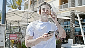 Young hispanic man dancing listening to music on smartphone at coffee shop terrace