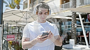 Young hispanic man dancing listening to music on smartphone at coffee shop terrace