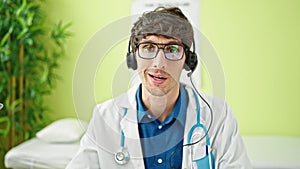 Young hispanic man doctor doing video call with laptop and headphones at the clinic