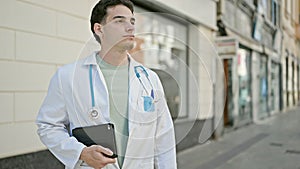 Young hispanic man doctor standing with serious expression holding touchpad at hospital