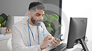 Young hispanic man doctor using smartphone and computer at clinic