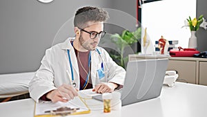 Young hispanic man doctor on video call prescribe pills writing clipboard at clinic